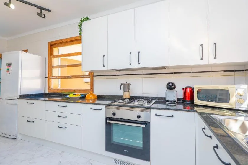 A bright kitchen with white cabinets, a refrigerator, and a countertop stove.