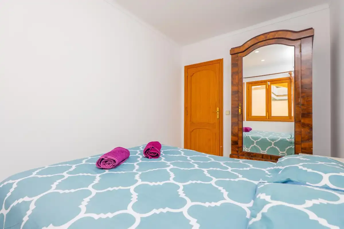 A bedroom with a patterned bedspread and a wooden-framed mirror.