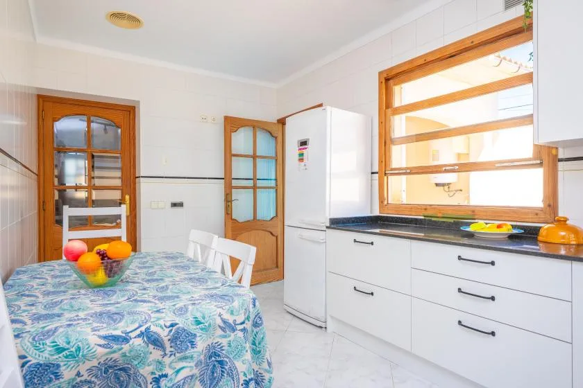 A bright kitchen and dining area with a patterned tablecloth and wood-framed windows.