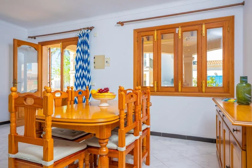 A dining area with a wooden table and chairs beside large windows.