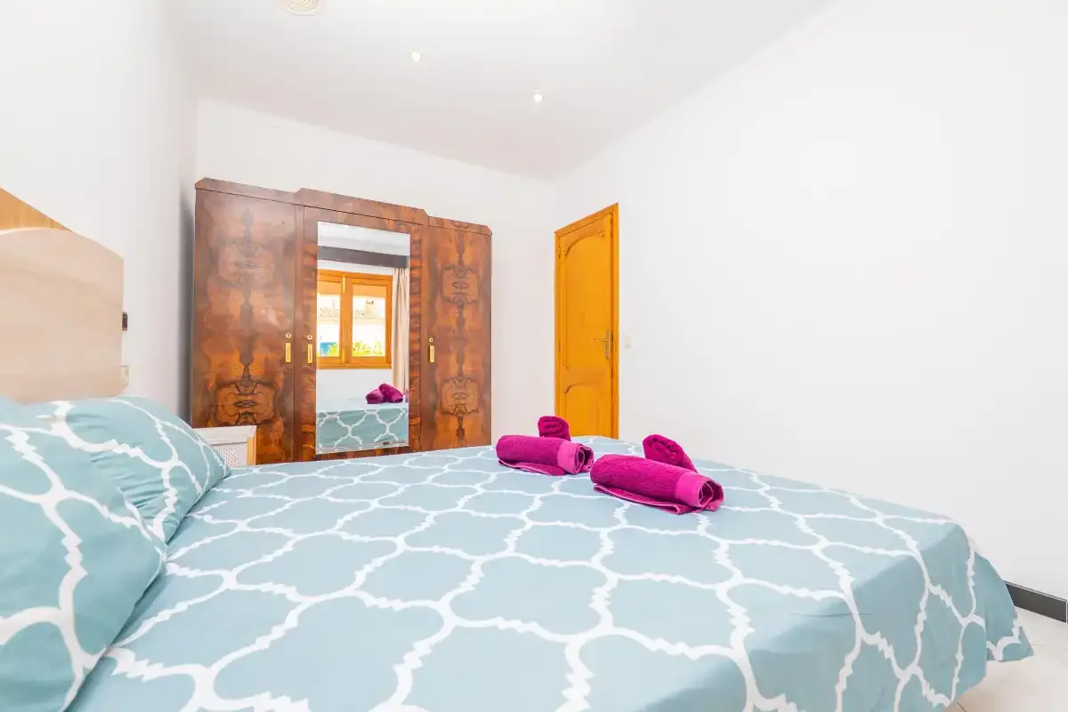 A bedroom with a patterned bedspread and a large wooden wardrobe.
