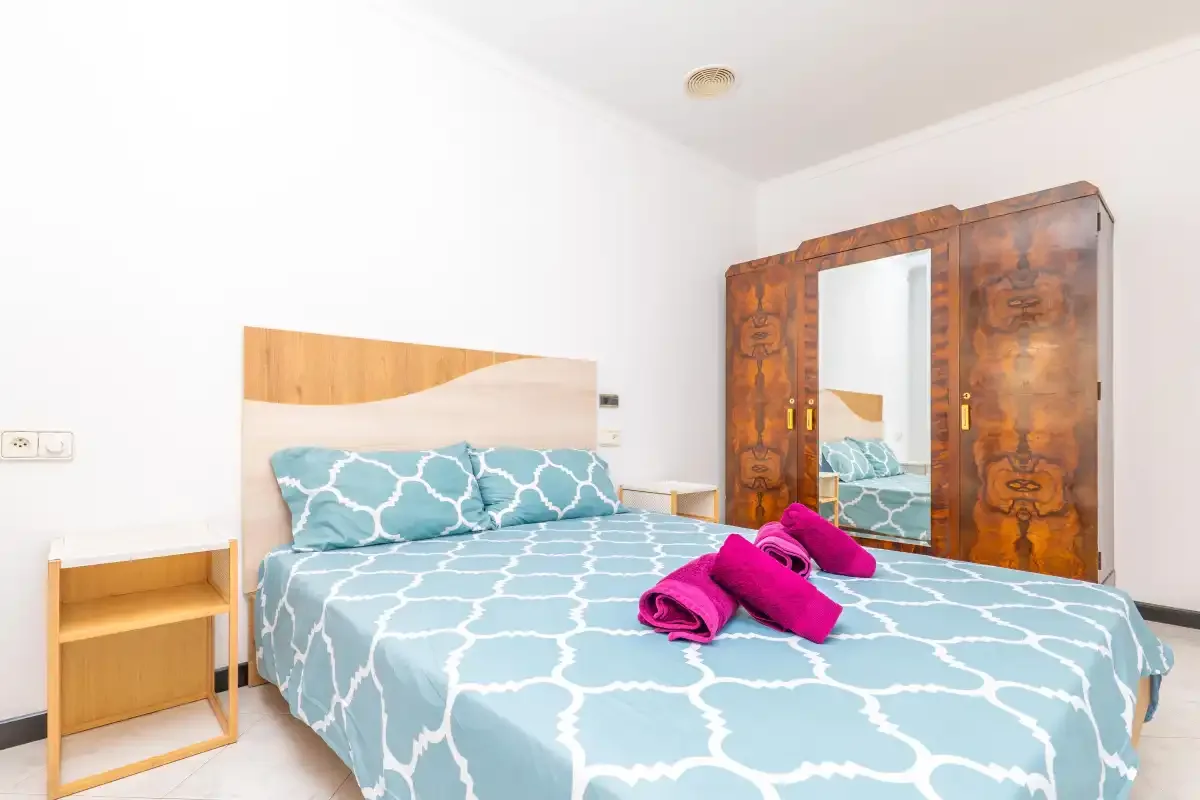 A bedroom with a double bed, patterned blue bedding, and a wooden wardrobe.