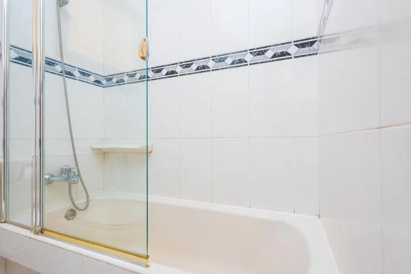 A tiled bathroom with a bathtub and glass shower screen.