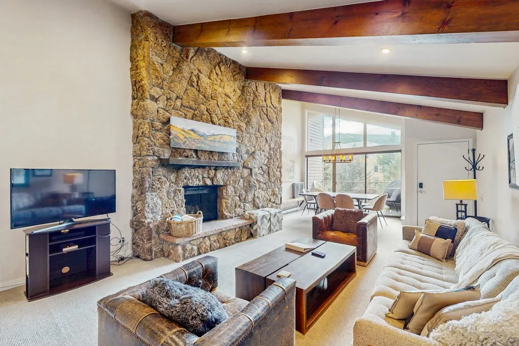 A living room with a stone fireplace, seating, and large windows.
