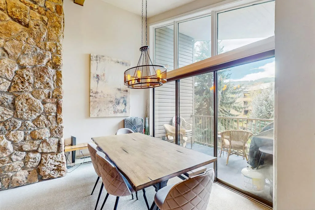 Un comedor luminoso con una mesa larga junto a grandes ventanales que dan a un patio.