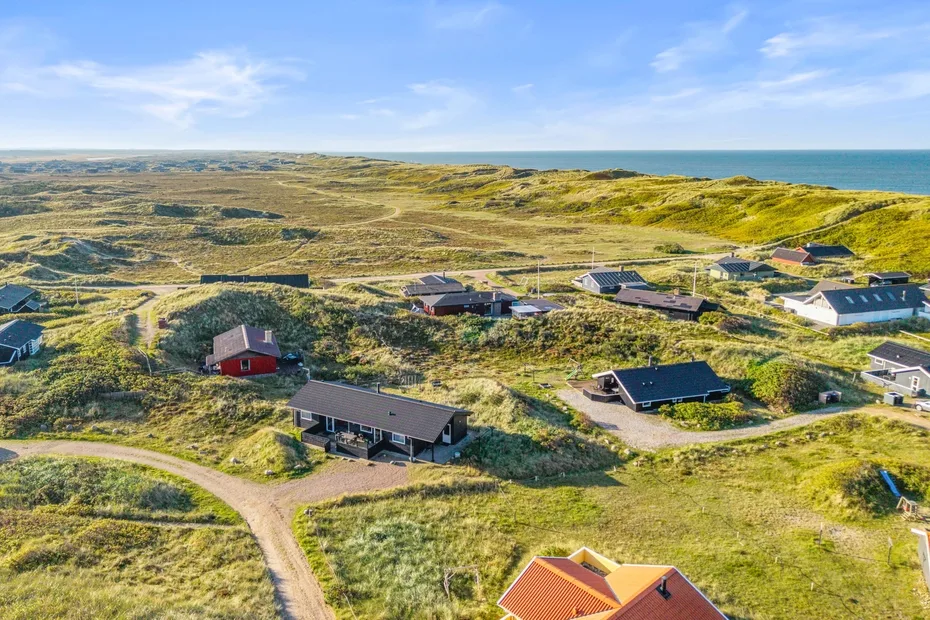 Vista aérea de casas dispersas entre dunas cubiertas de hierba junto a la costa.
