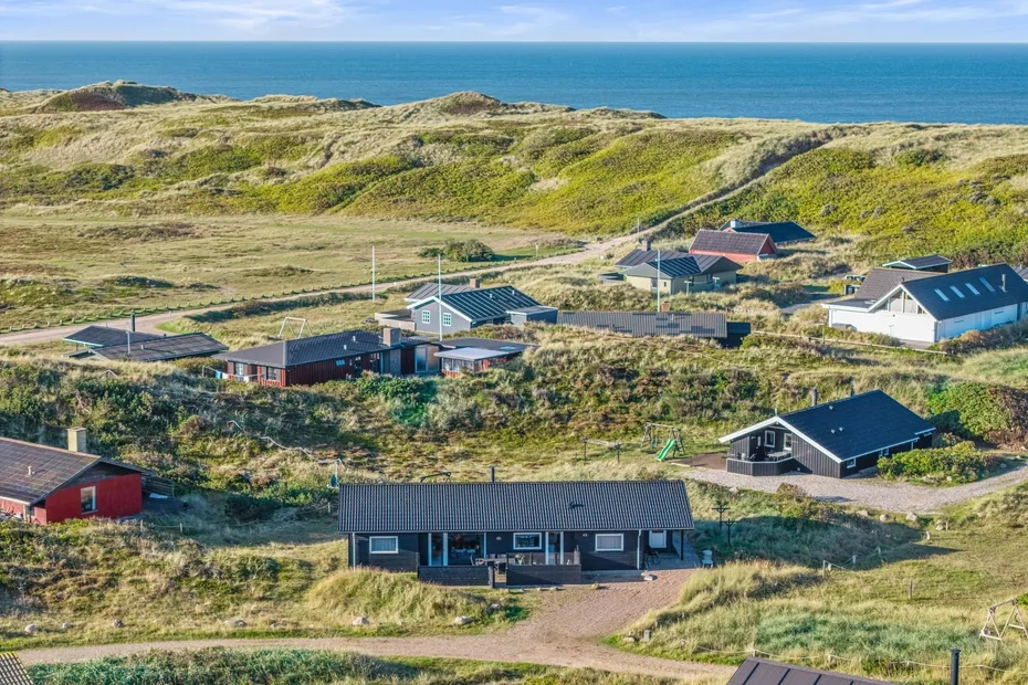 Un conjunto de casas costeras se encuentra entre dunas cubiertas de hierba junto al mar.