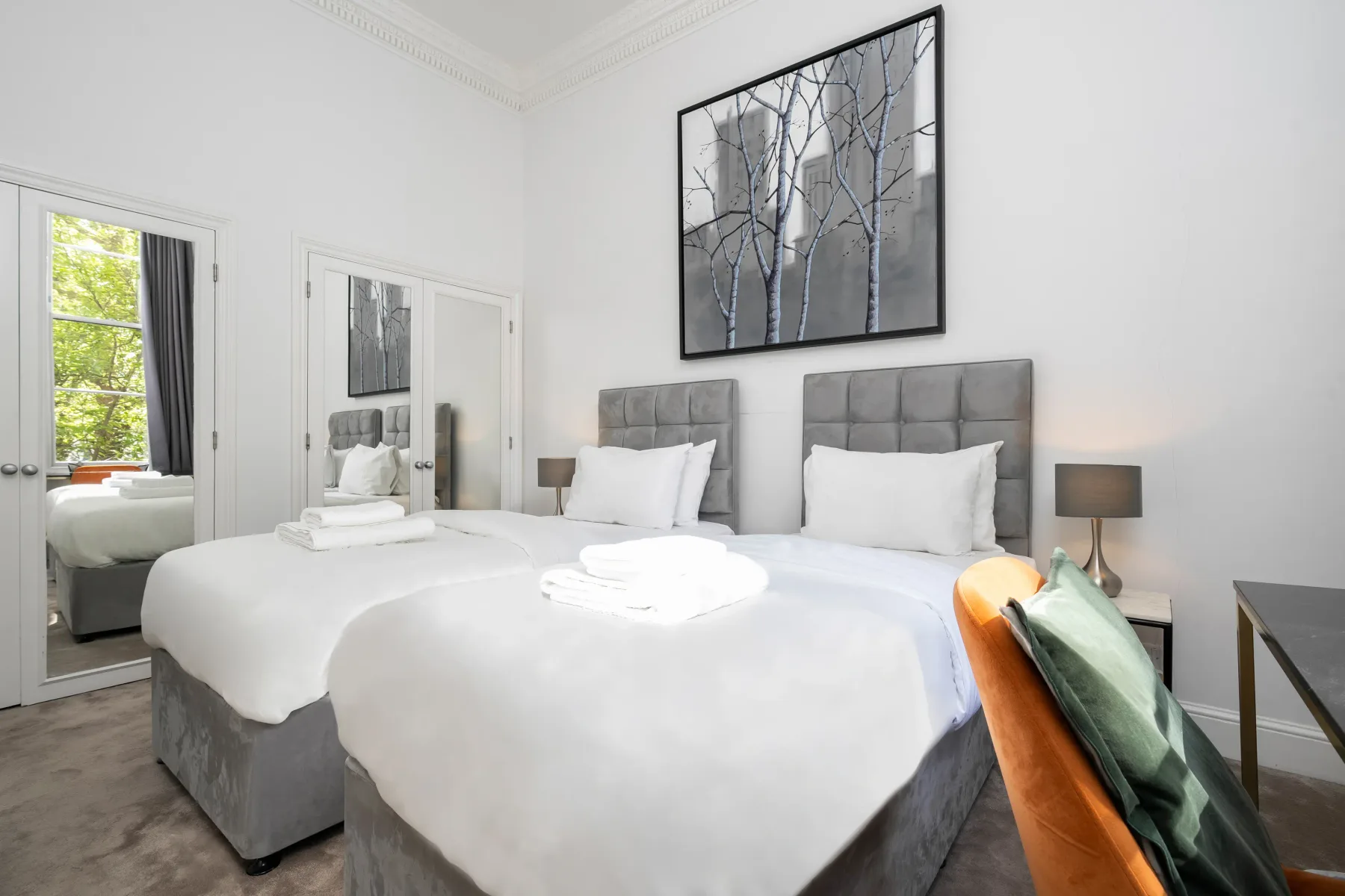 Un dormitorio luminoso con dos camas, ropa de cama blanca y cuadros enmarcados.