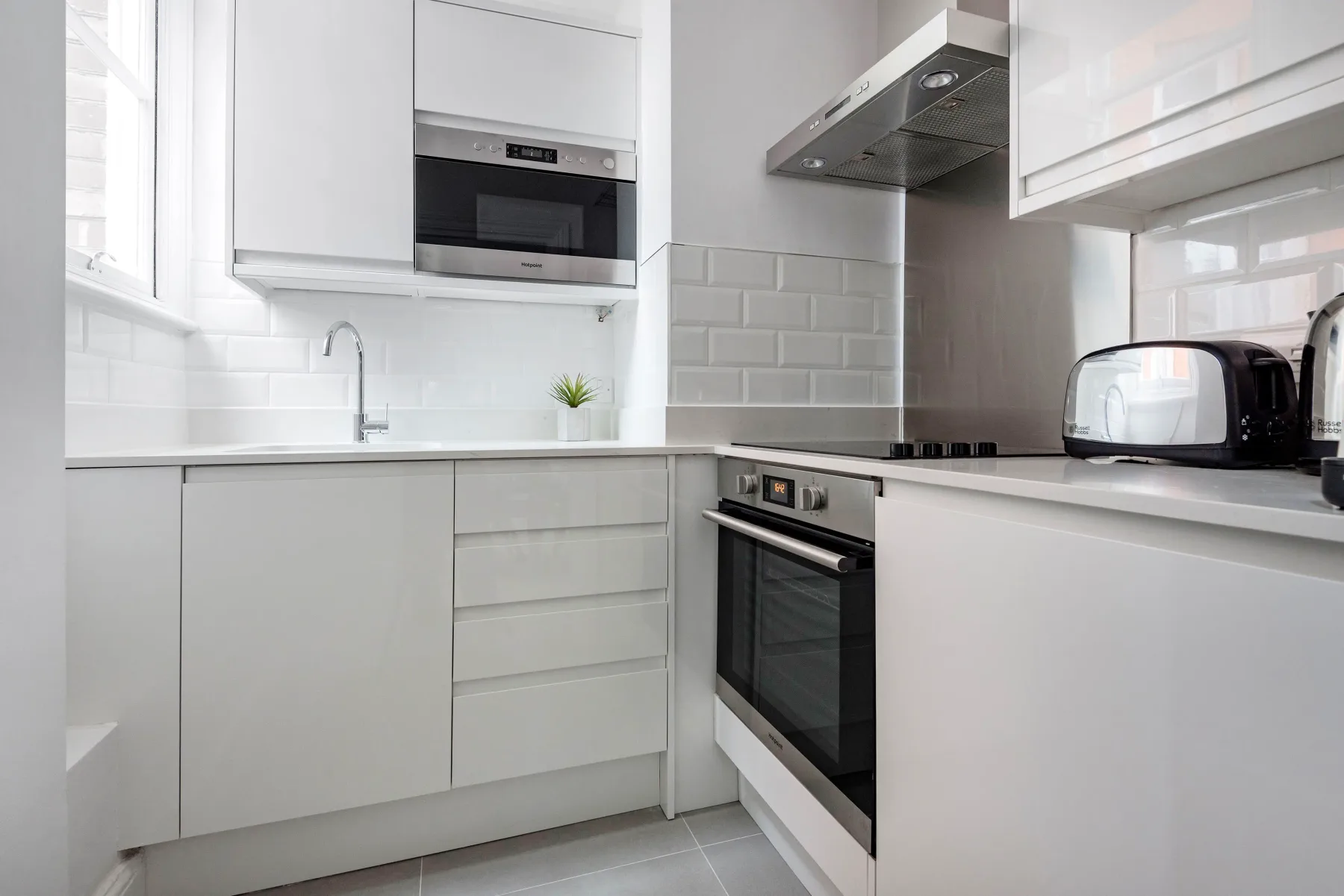 Una cocina blanca y luminosa con electrodomésticos integrados y un salpicadero de azulejos.