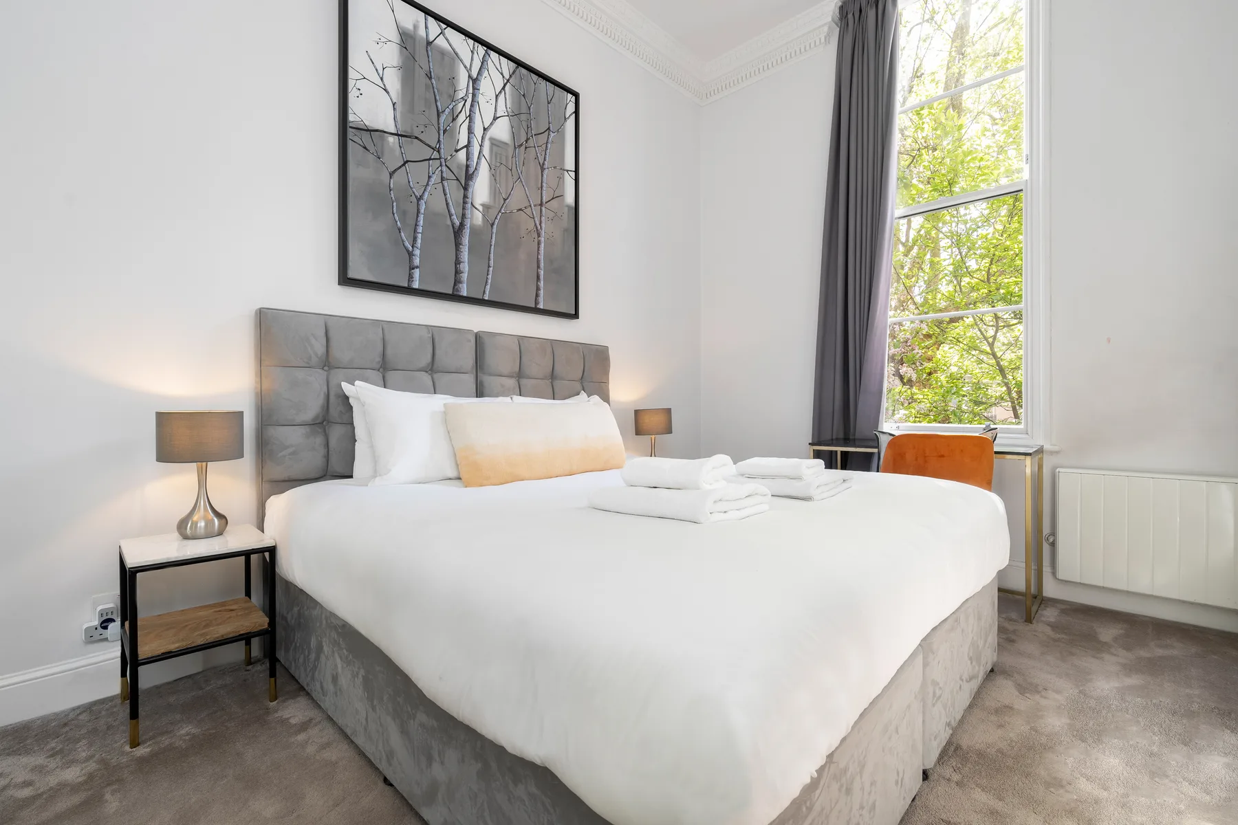 Un dormitorio luminoso con una cama bien hecha y una ventana grande.