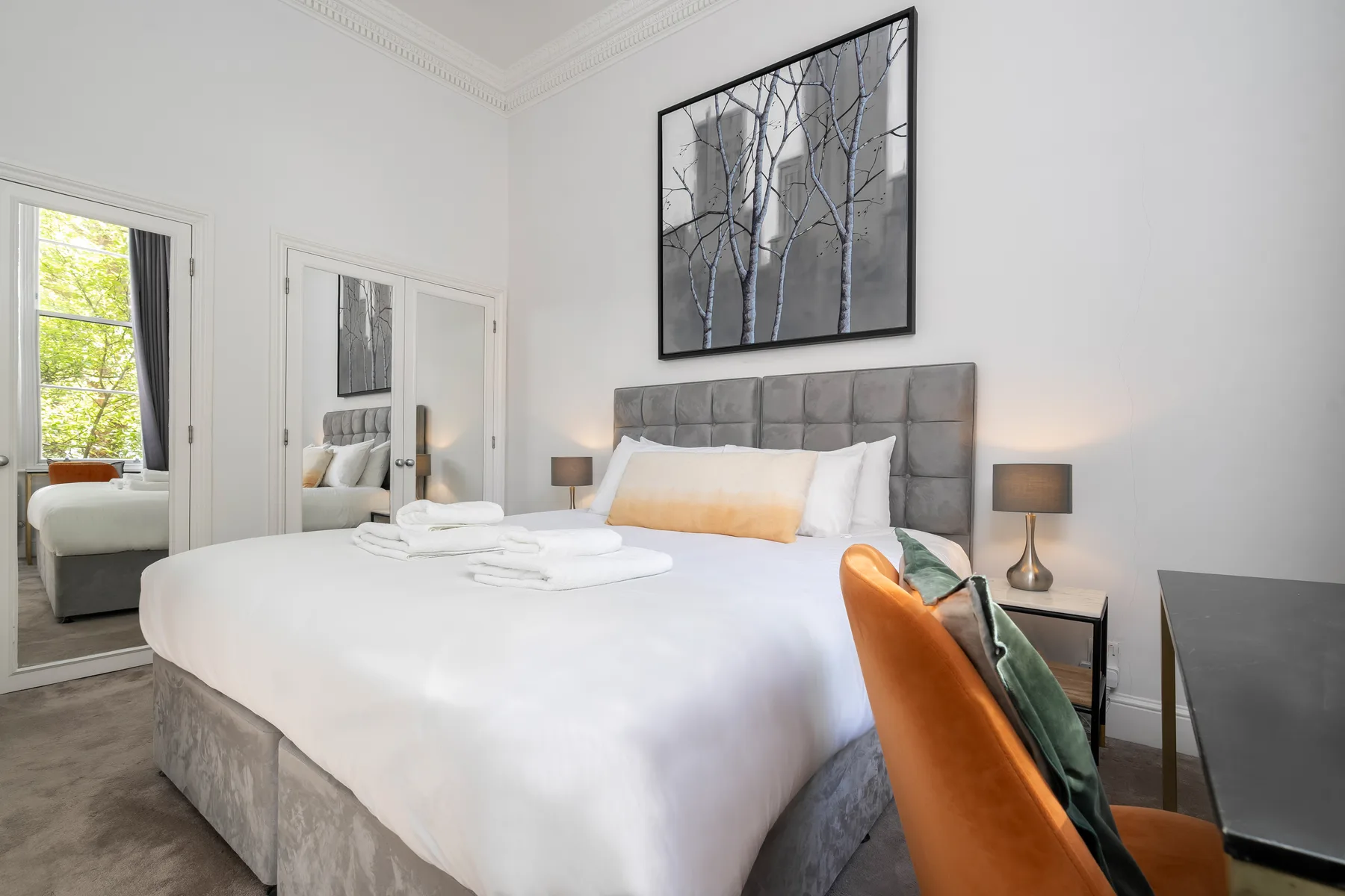 Un dormitorio luminoso con una cama bien tendida y un cuadro sobre el cabecero.