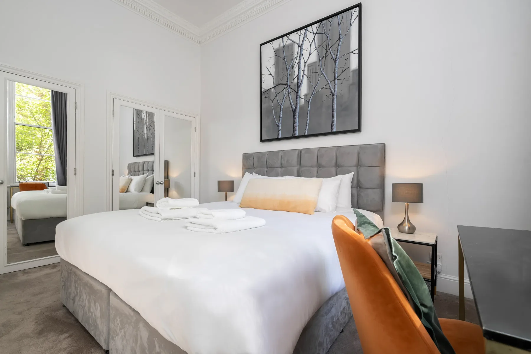 Un dormitorio luminoso con una cama bien hecha y un cuadro sobre el cabecero.