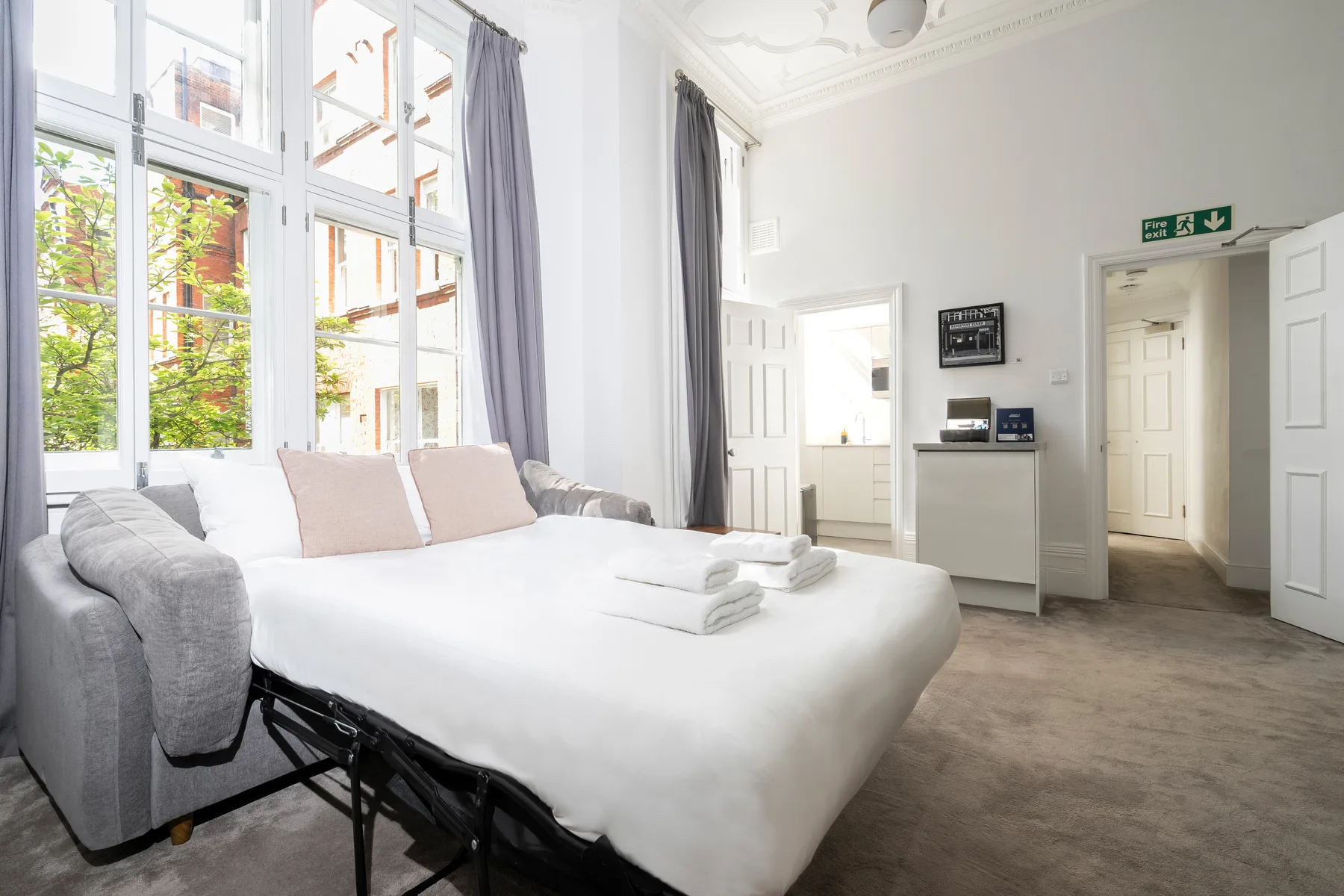 Un dormitorio luminoso con una cama grande junto a ventanas altas.