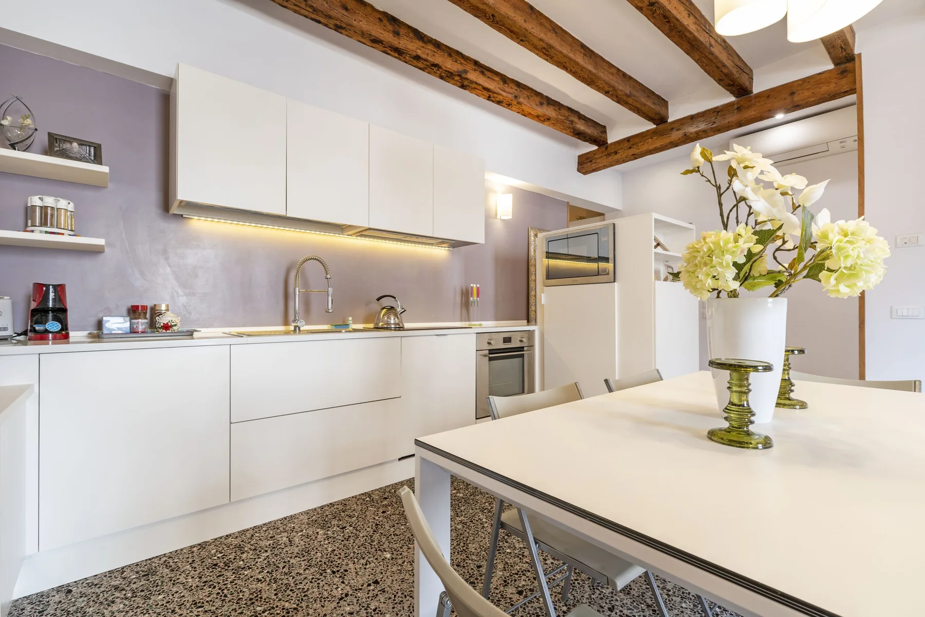 A bright kitchen and dining area with white cabinetry and a table set with flowers.