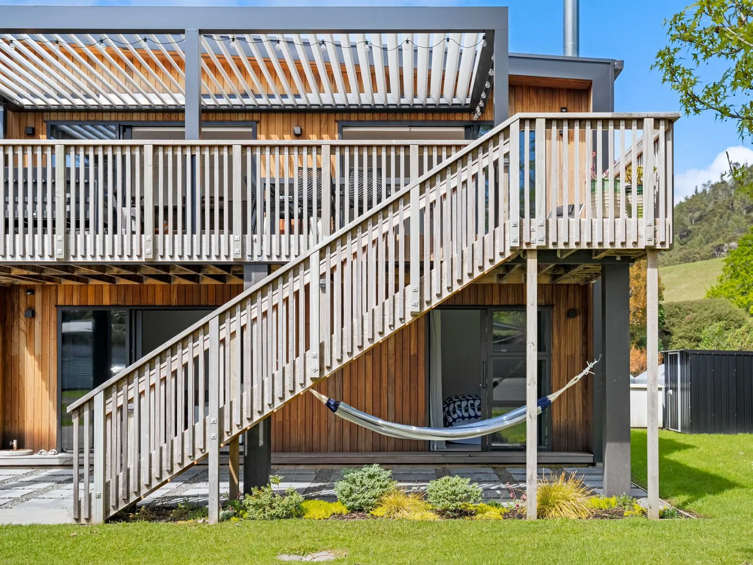 An outdoor area with a building, stairs, and a hammock at The Cove Escape - Cooks Beach