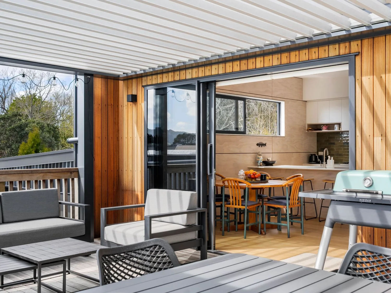 A patio with outdoor seating and a view of the kitchen at The Cove Escape - Cooks Beach