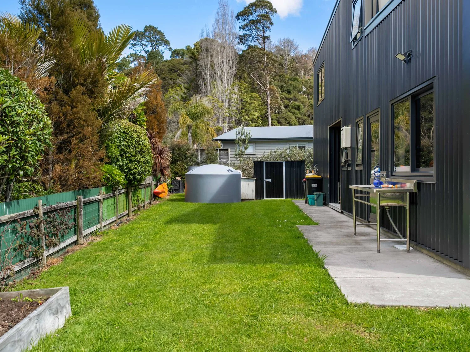 A garden with a water tank and table at The Cove Escape - Cooks Beach