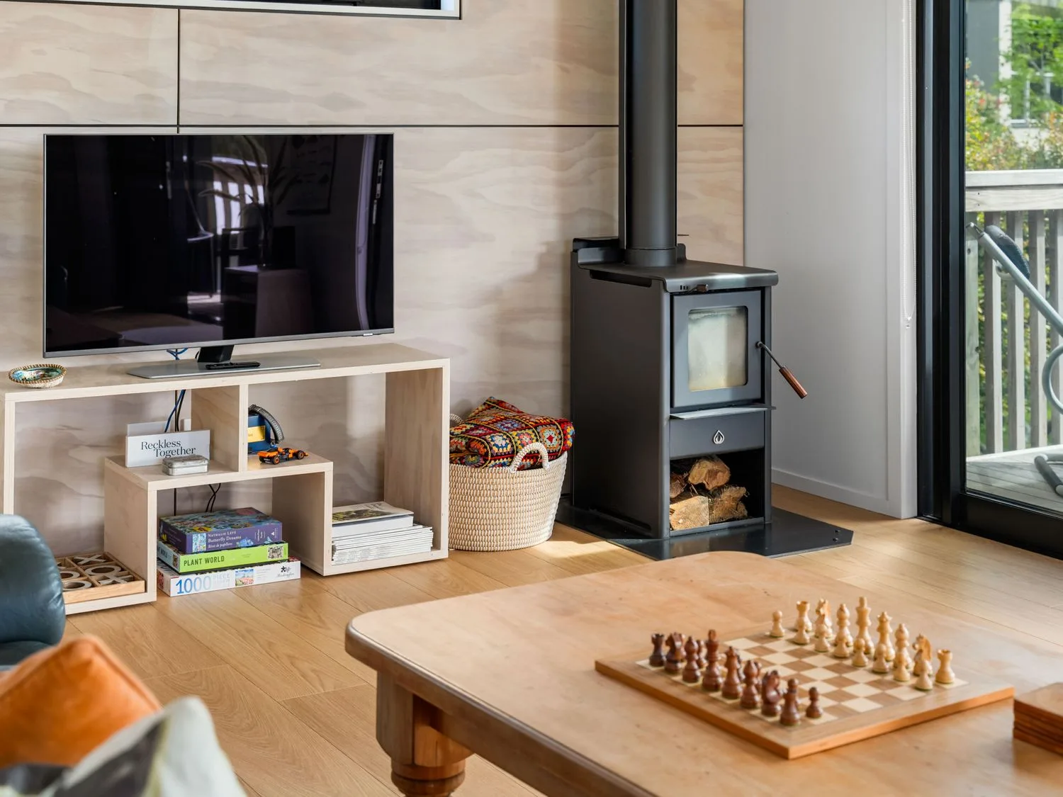 Una sala de estar con un televisor, una estufa de leña y un juego de ajedrez en The Cove Escape - Cooks Beach Holiday Home