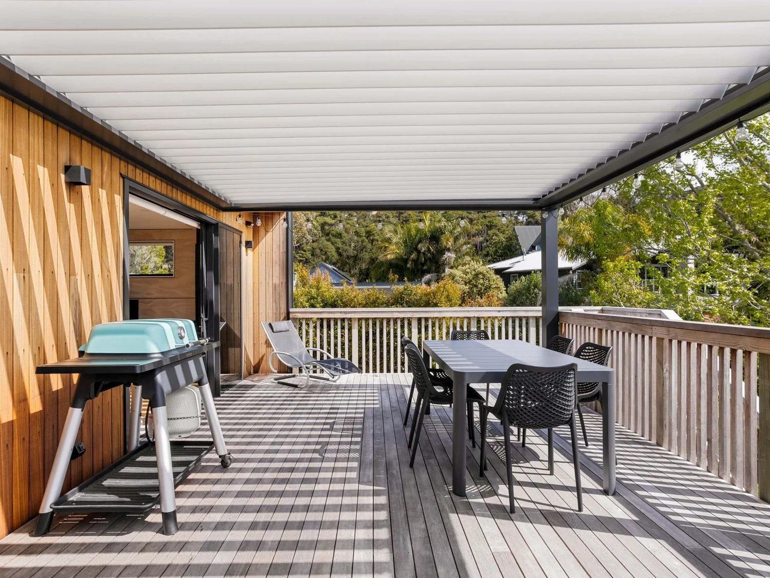 A covered outdoor deck with a dining table and seating overlooks greenery.