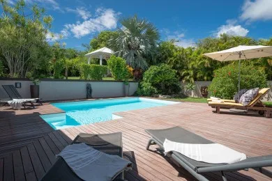 An outdoor pool sits beside a spacious wooden deck with lounge seating and greenery.