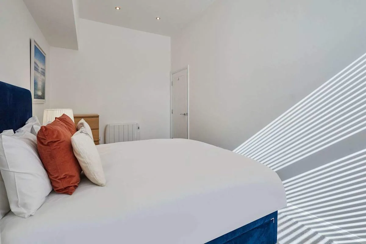 Un dormitorio con una cama tendida y luz solar proyectando sombras a rayas en la pared.