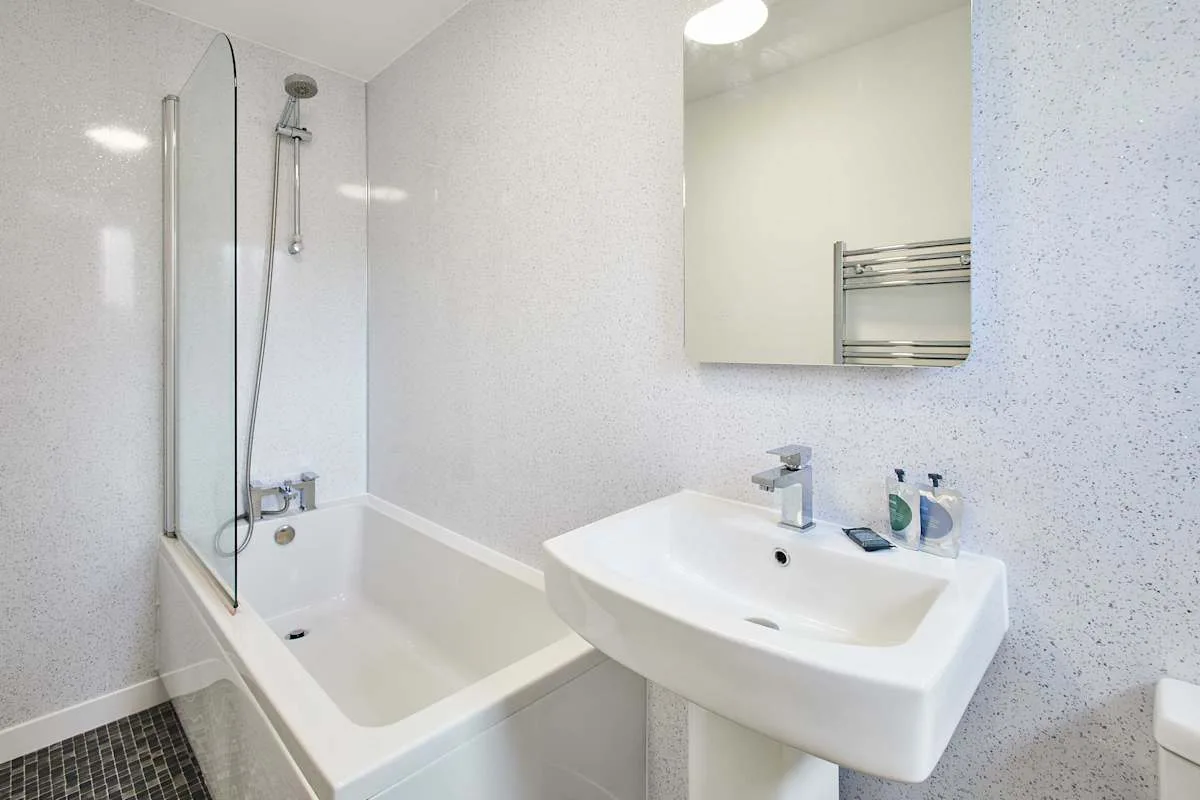 Un baño con bañera y mampara de vidrio junto a un lavabo.