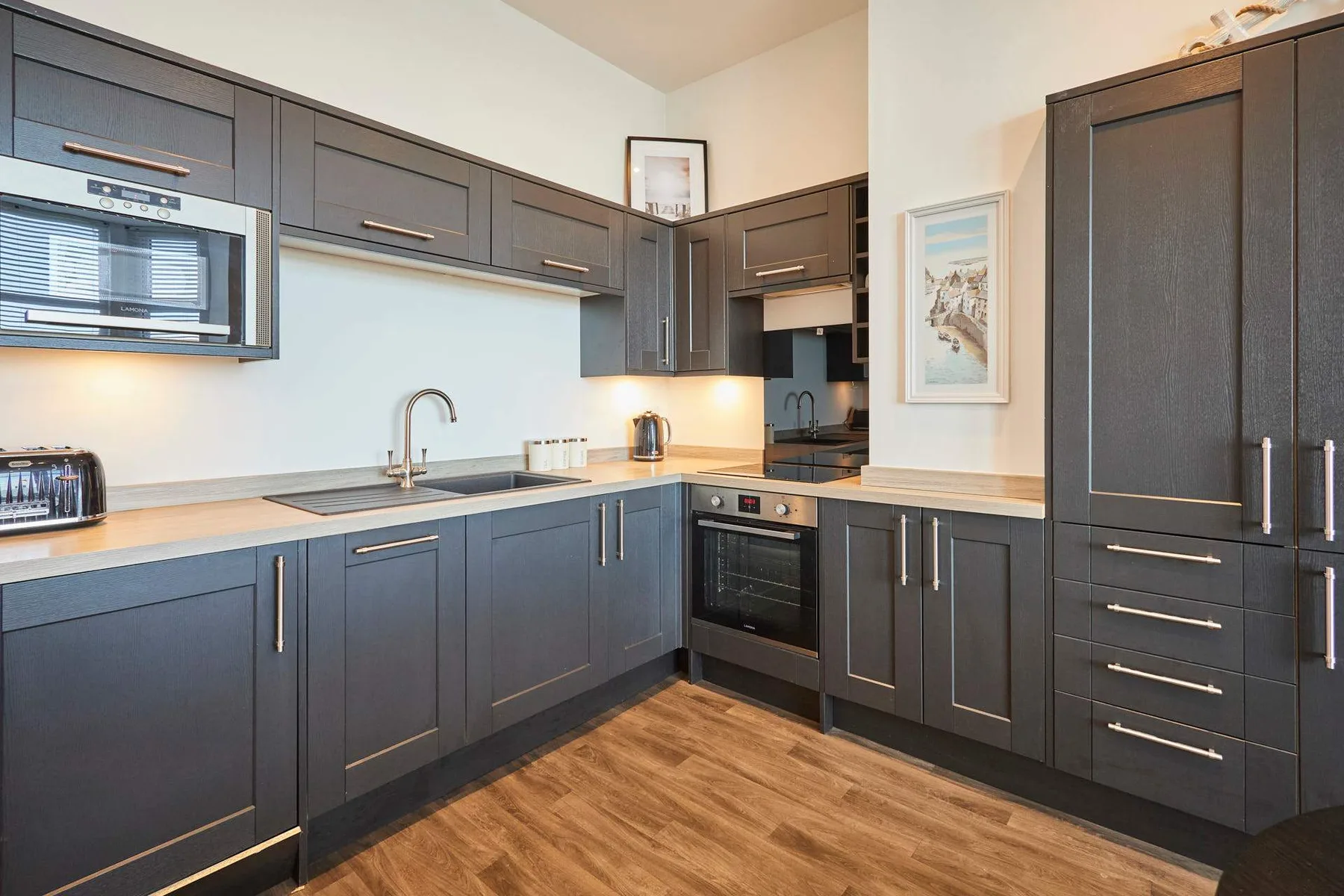 A modern kitchen with dark cabinetry, light countertops, and wood flooring.