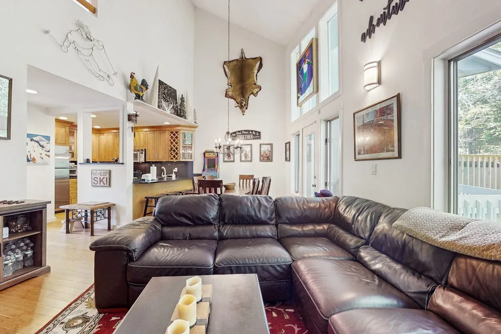 A spacious living room features leather seating, a coffee table, and tall windows.