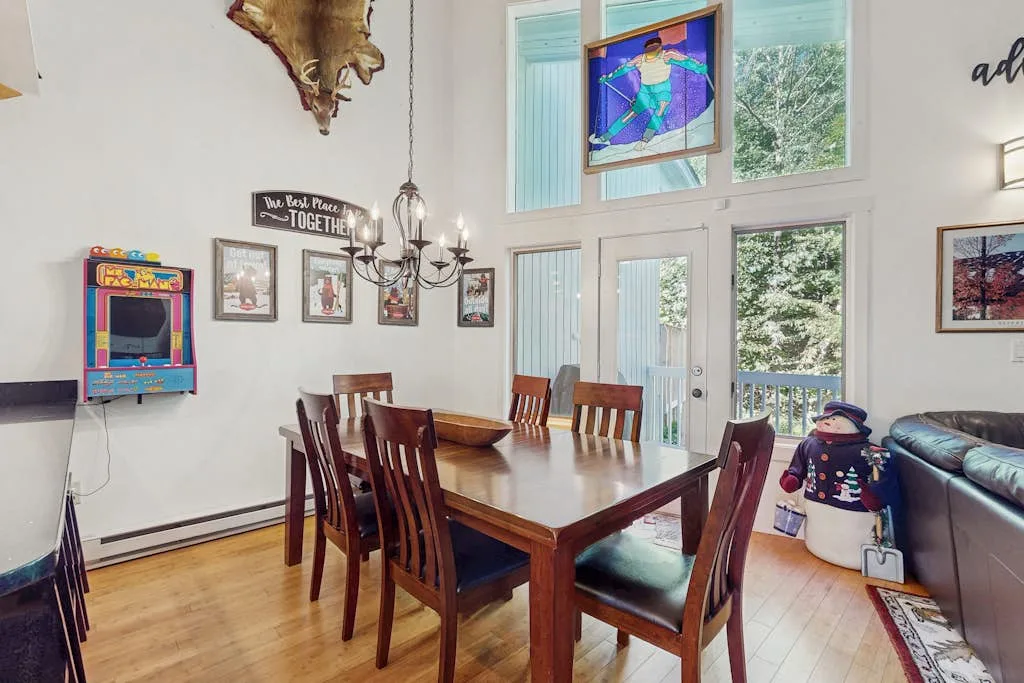 A dining area with a wooden table and chairs beside tall windows and glass doors.