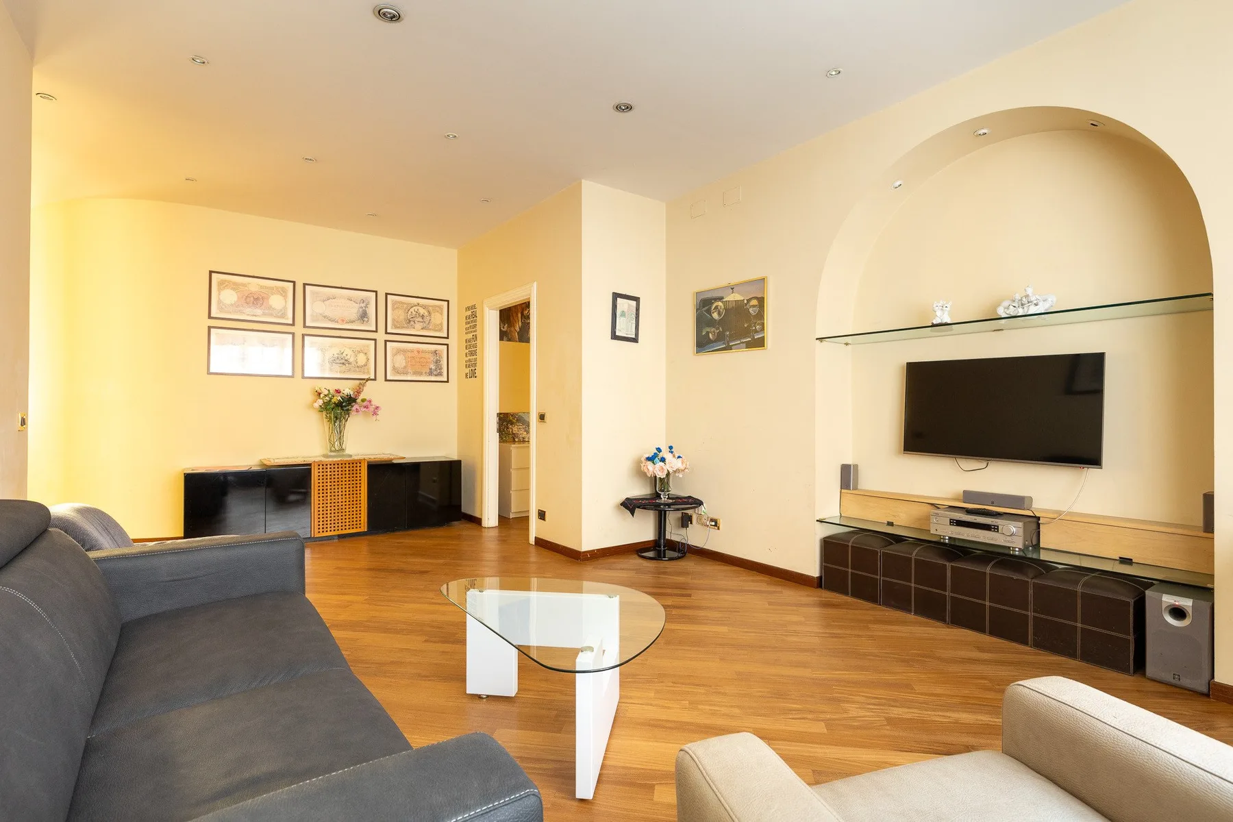 Una sala de estar con asientos, una mesa de centro de vidrio y un televisor integrado en la pared.