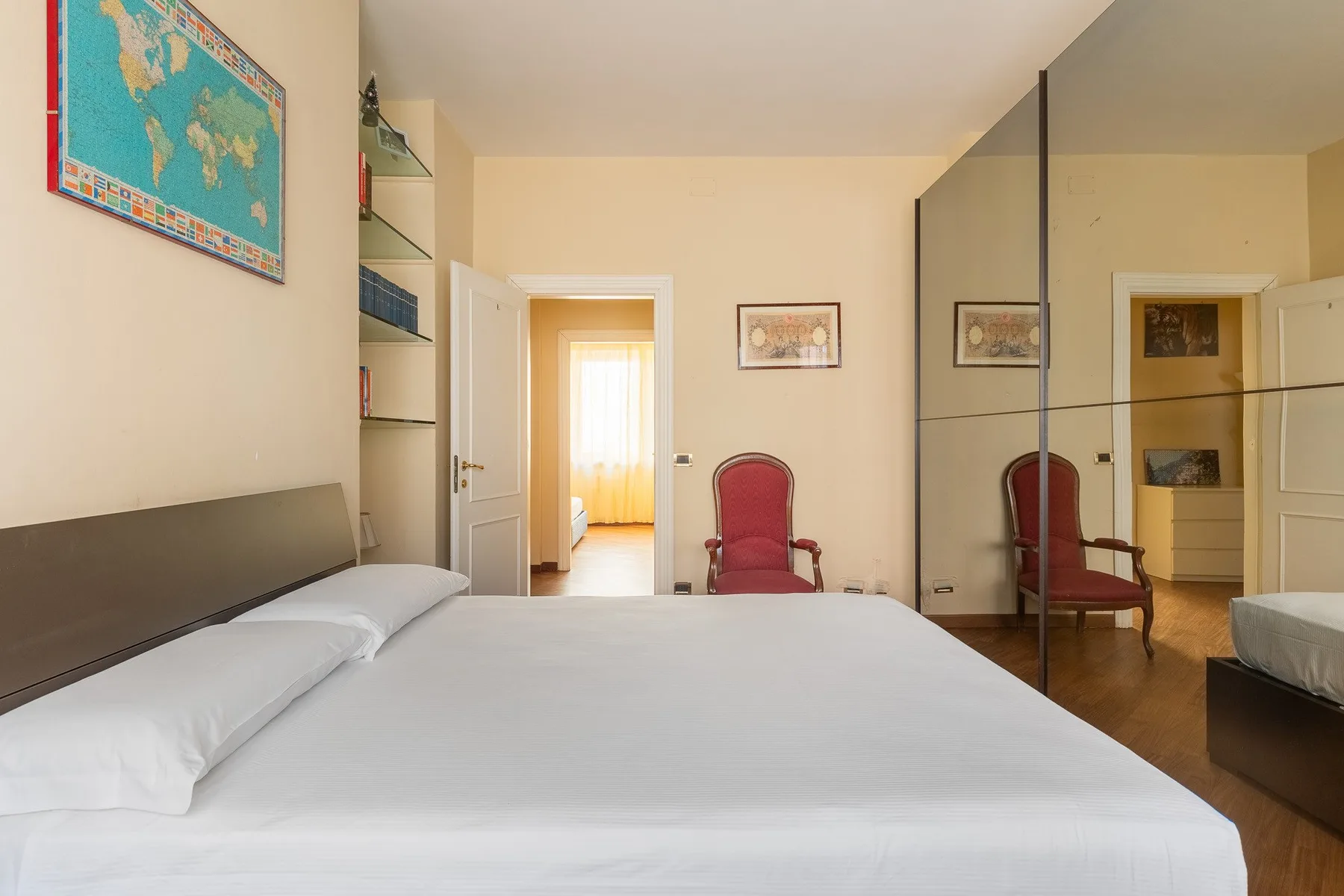 Un dormitorio con una cama grande, un sillón rojo y puertas de armario con espejo.