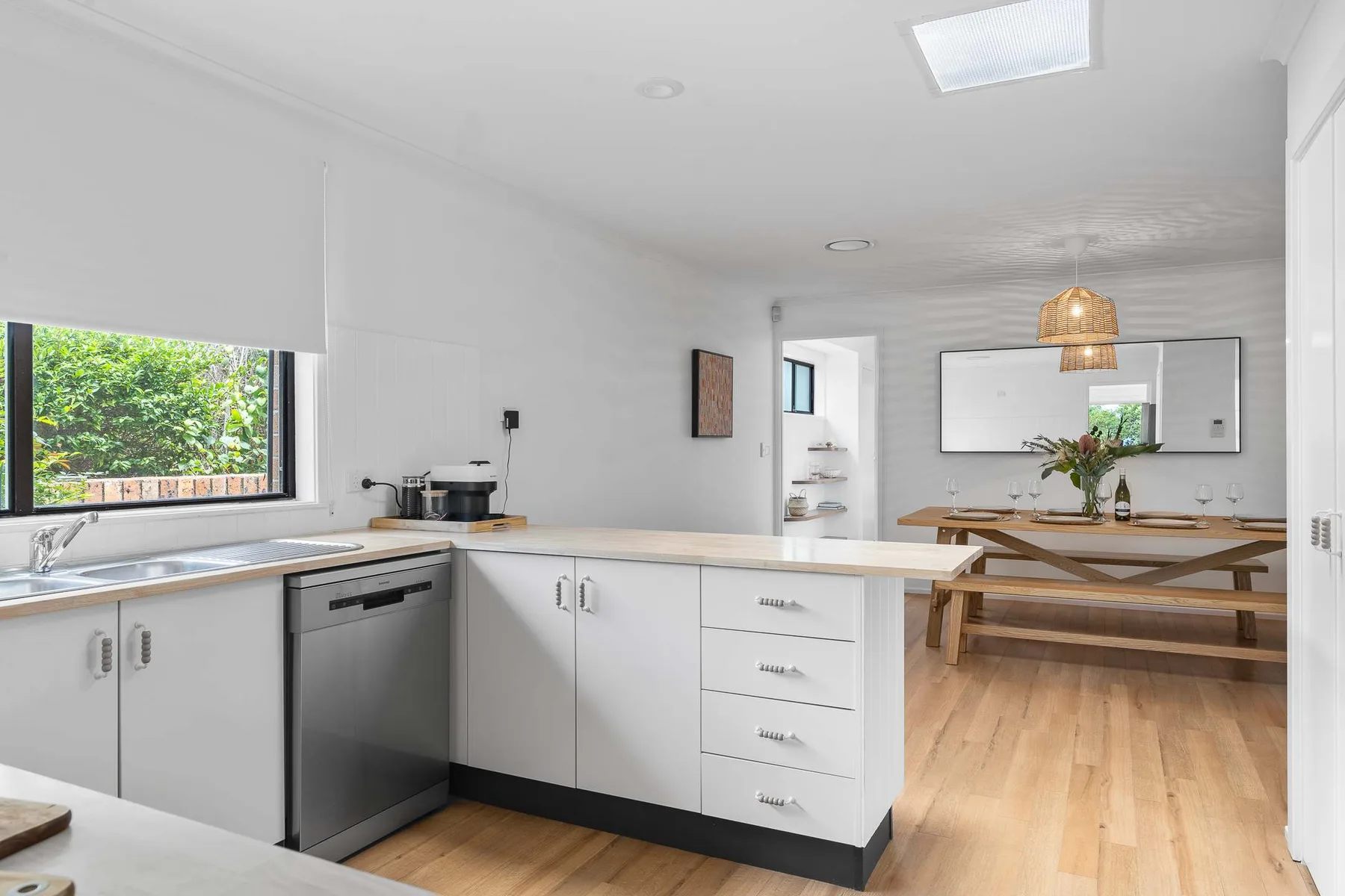 A bright kitchen opens into a dining area with a wooden table.
