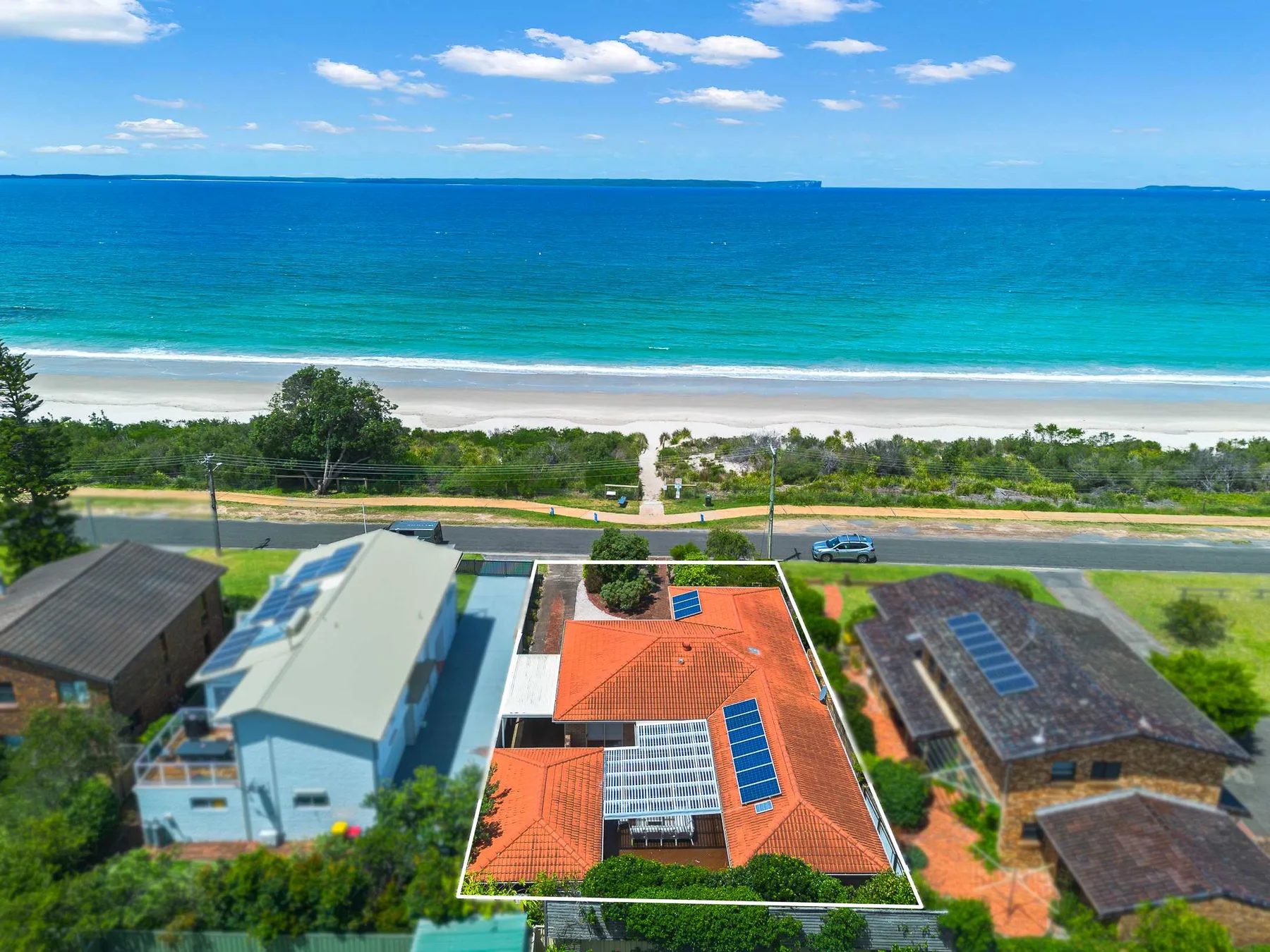Aerial view of a coastal neighborhood beside a sandy beach and turquoise sea.