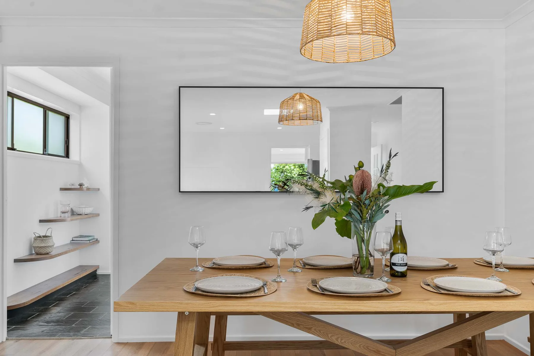 A dining table is set with plates and a floral centerpiece beneath a pendant light.