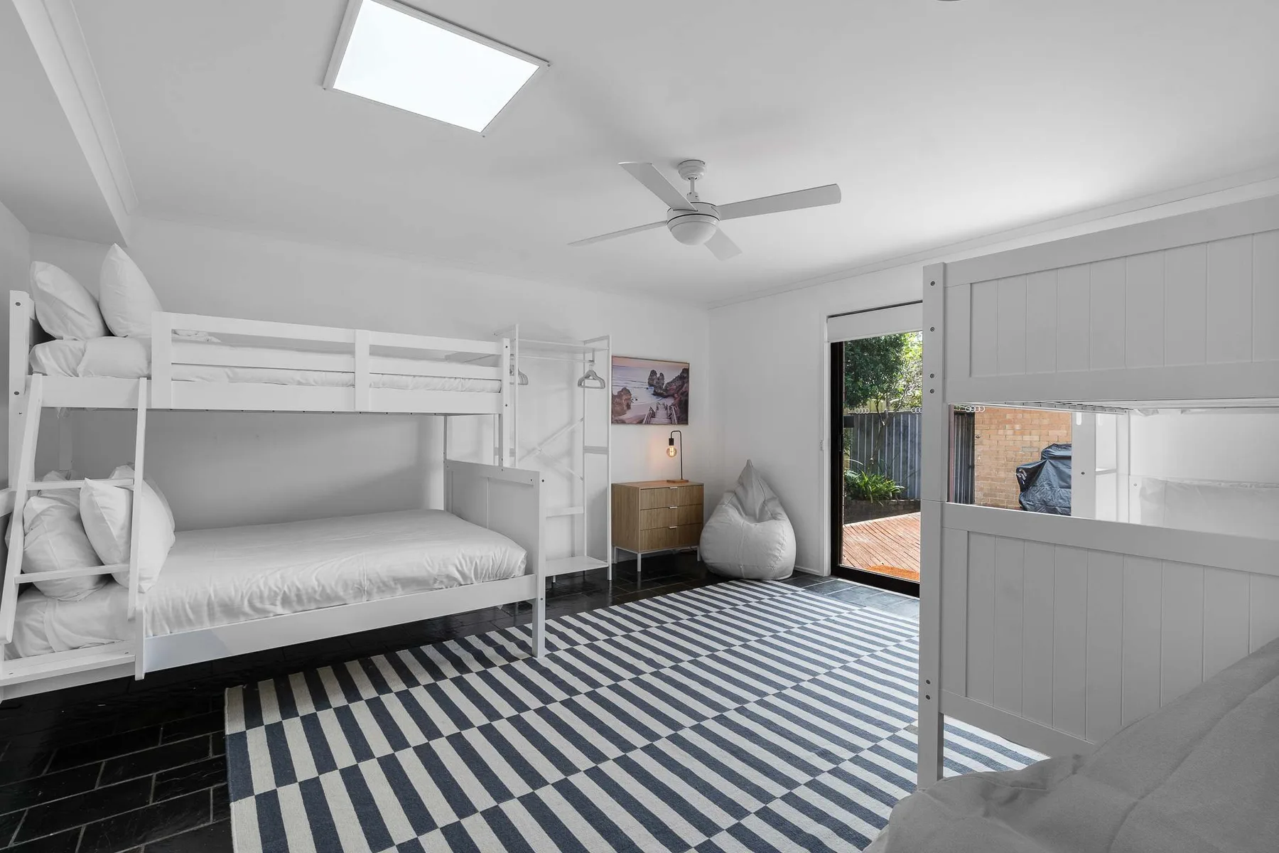 A bright bedroom with bunk beds, a striped rug, and an open door to the outside.
