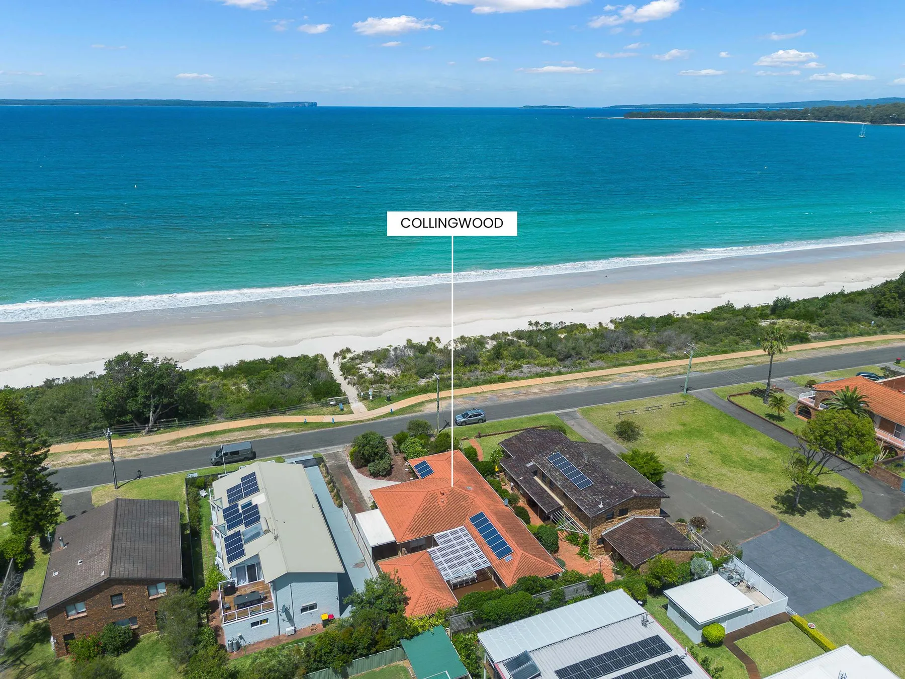 Aerial view of a coastal neighborhood beside a sandy beach and turquoise water.