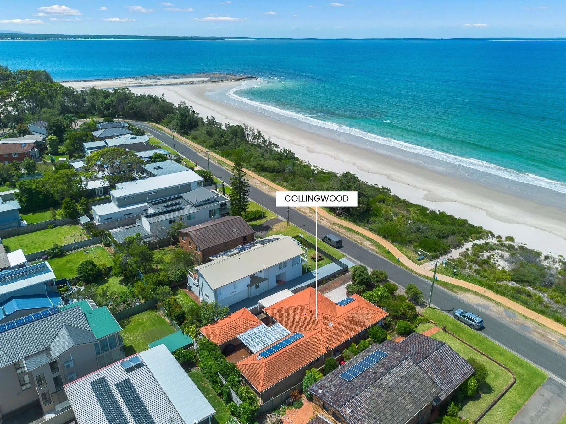 An aerial view of homes beside a curving sandy beach and turquoise water.