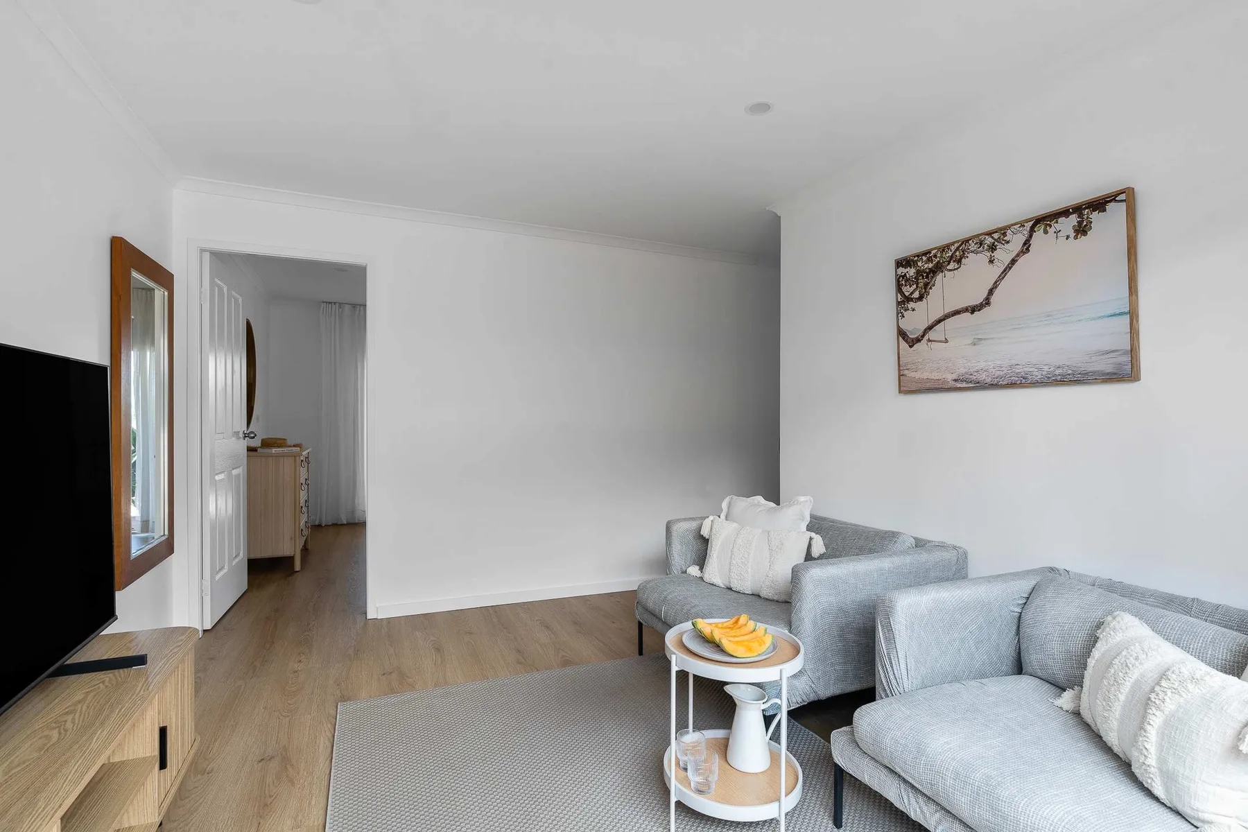 A bright living room with gray seating, a small table, and framed wall art.