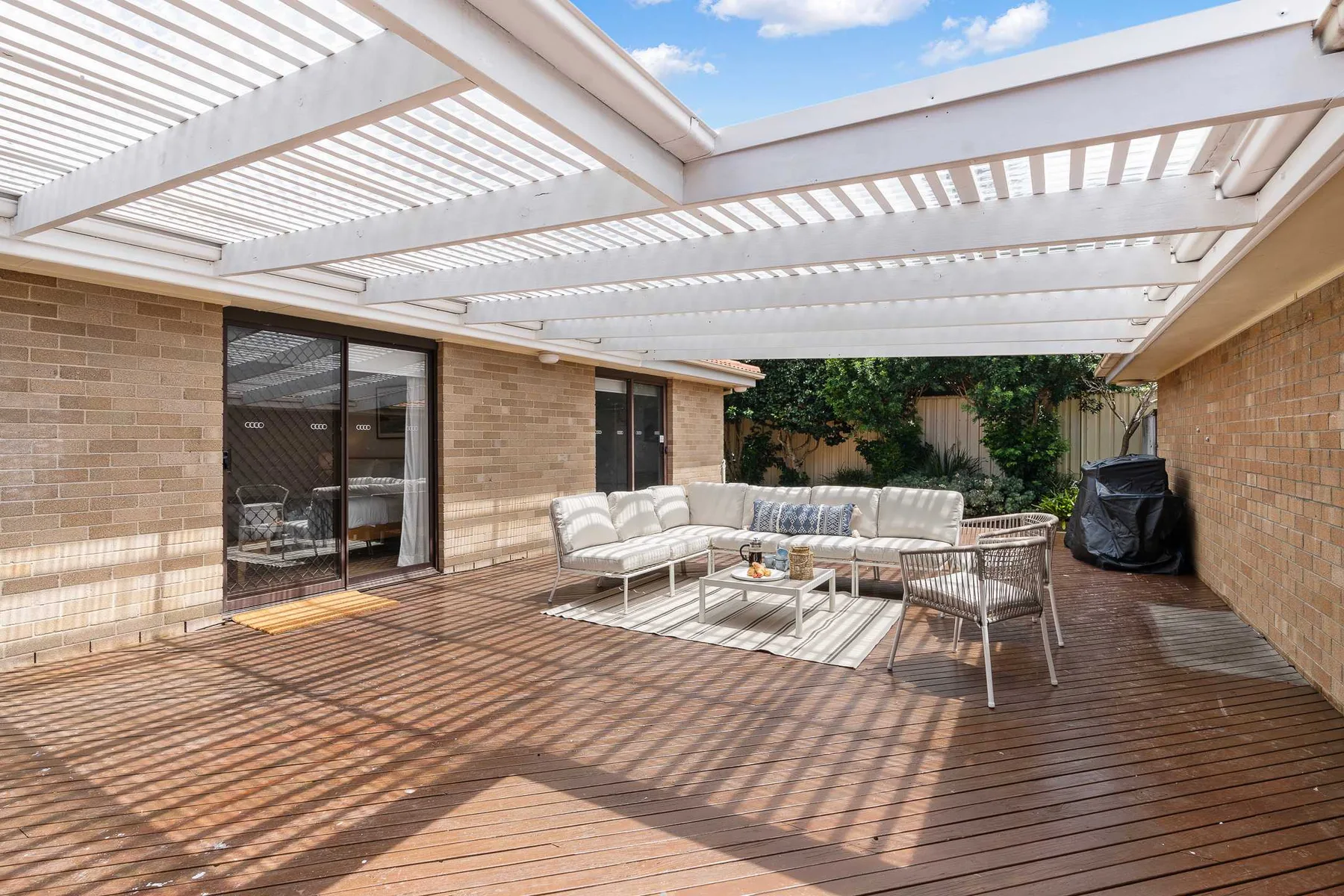 A furnished outdoor patio beneath a white pergola, with seating and a table.