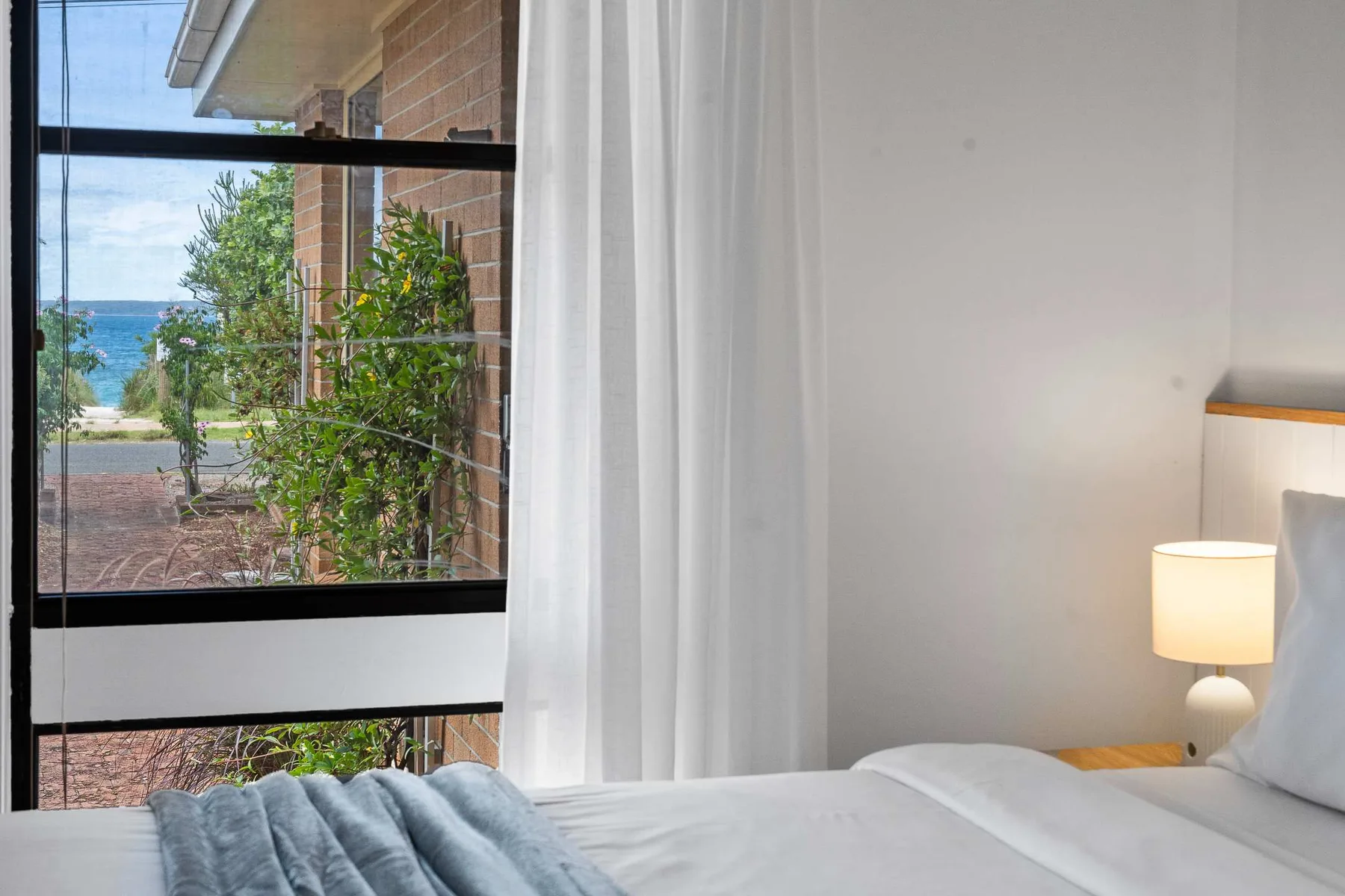 Bedroom with a bed beside a large window overlooking greenery and water.