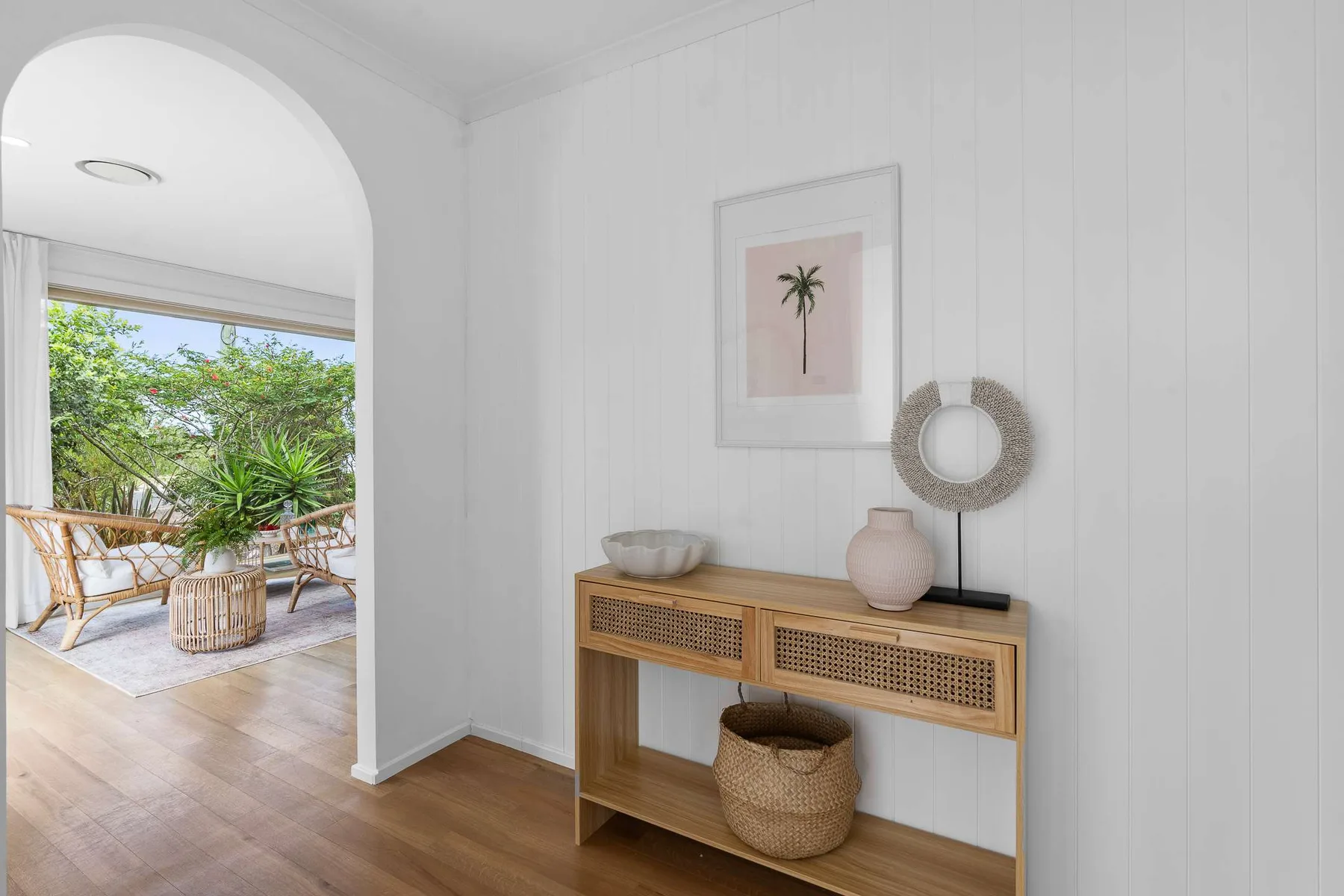 A bright entryway features a wooden console table and a view of a leafy patio.