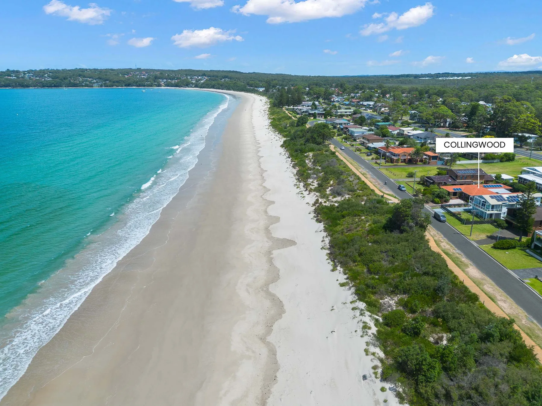 Aerial view of a sandy beach beside turquoise water and coastal homes.