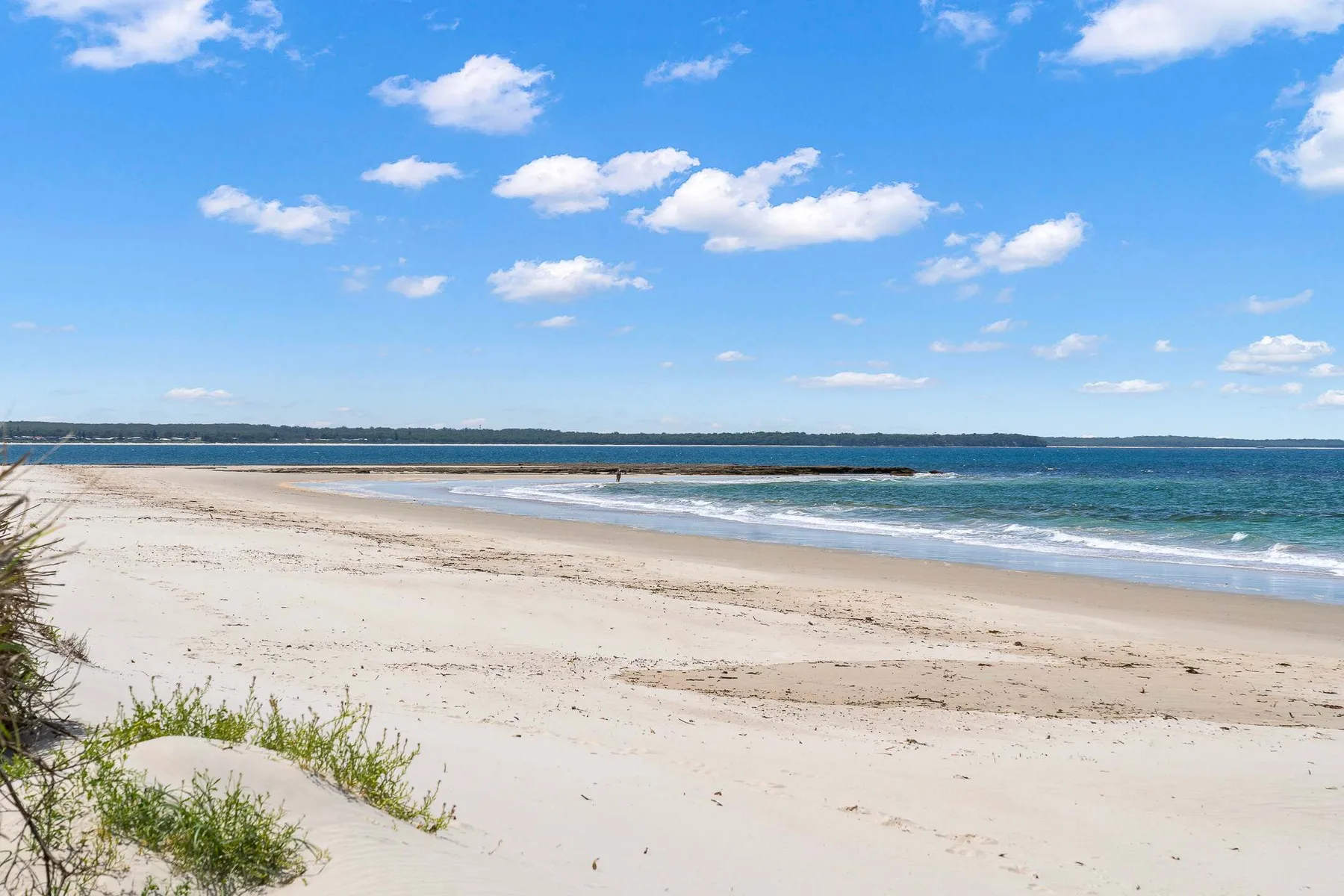A wide sandy beach meets calm blue water beneath a partly cloudy sky.