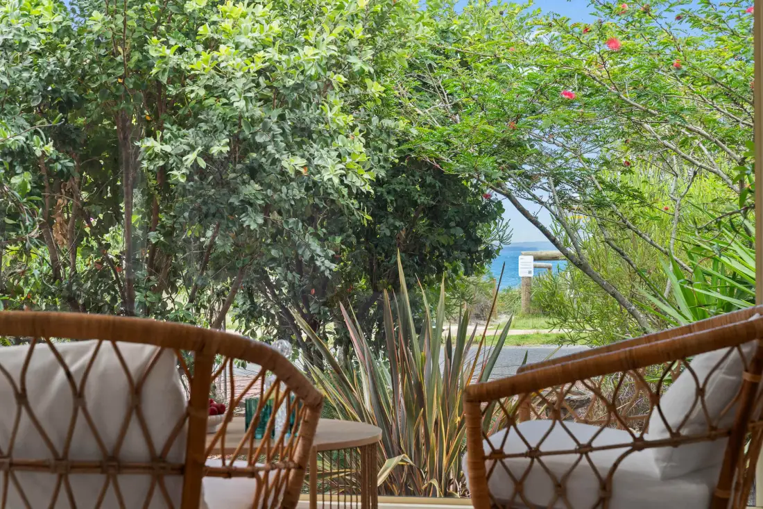 Outdoor seating overlooks a leafy garden with a glimpse of the water beyond.