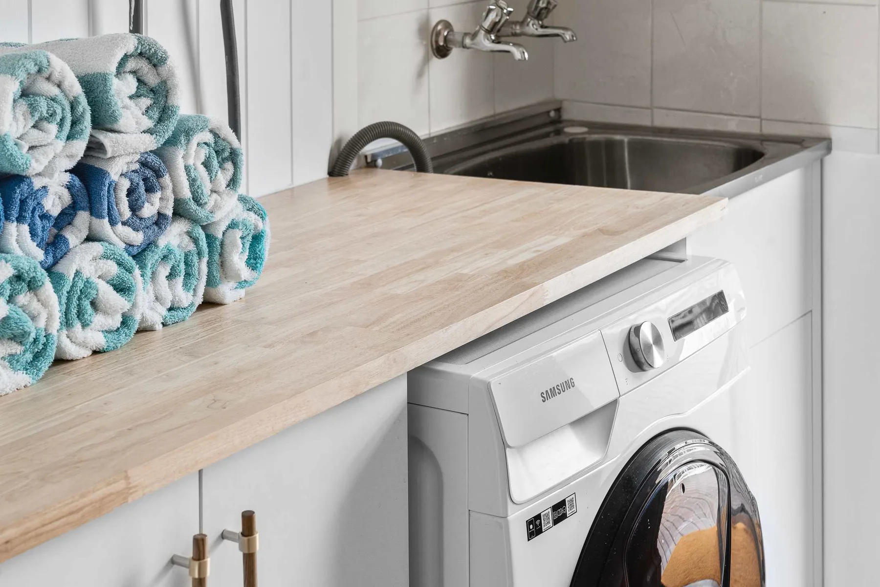 A laundry area with a washing machine beneath a counter beside a sink.