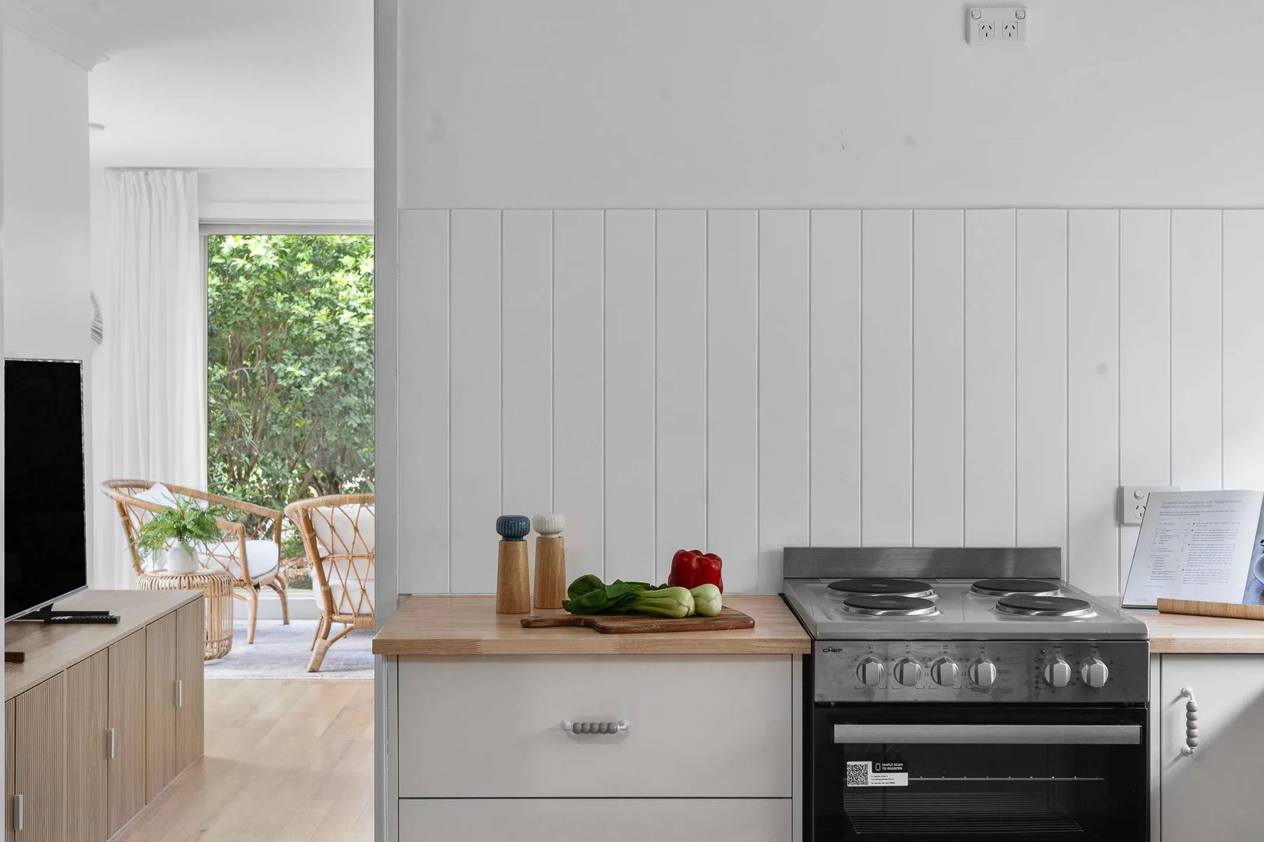 A bright kitchen with a cooktop and a leafy view through the window.