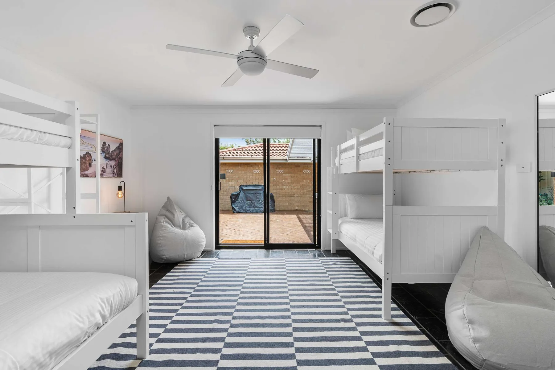 A bright bedroom with bunk beds, a striped rug, and a glass door opening to a patio.
