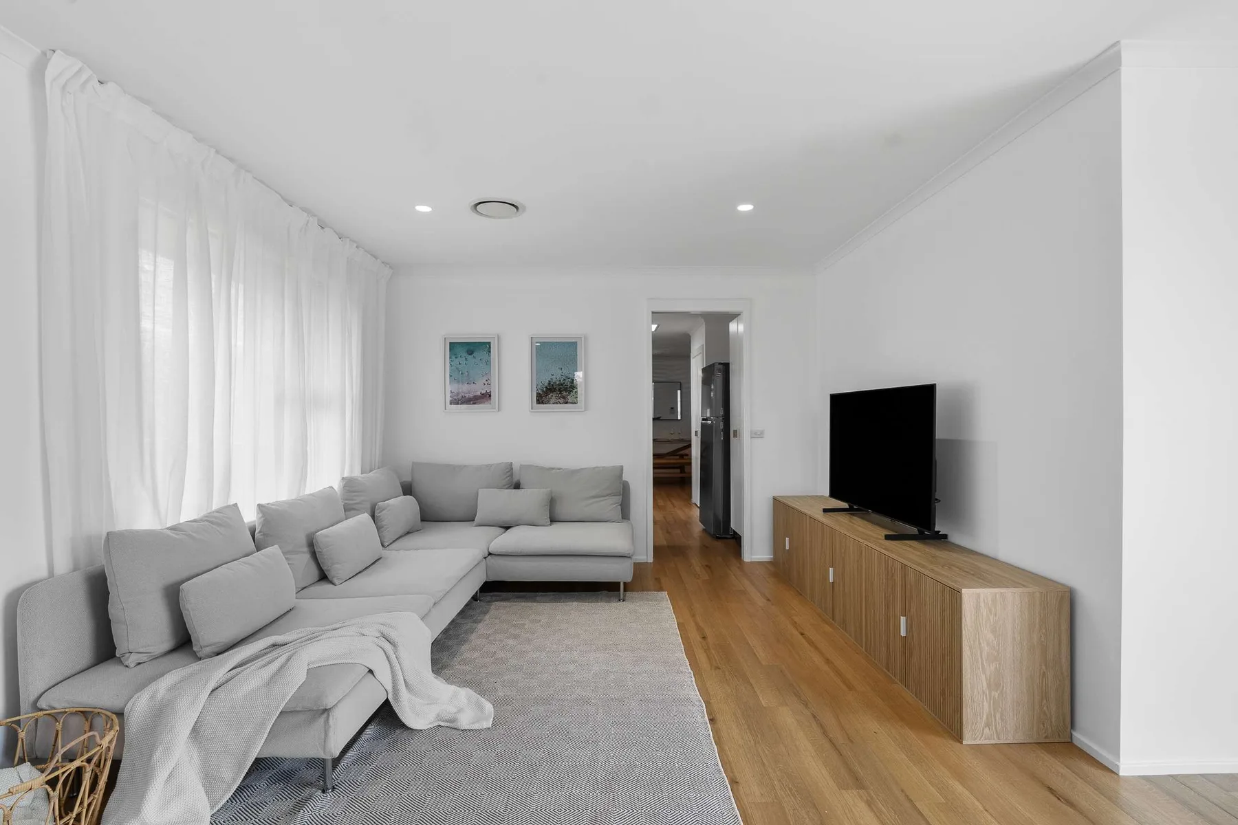 A bright living room with gray seating, a television, and light wood flooring.