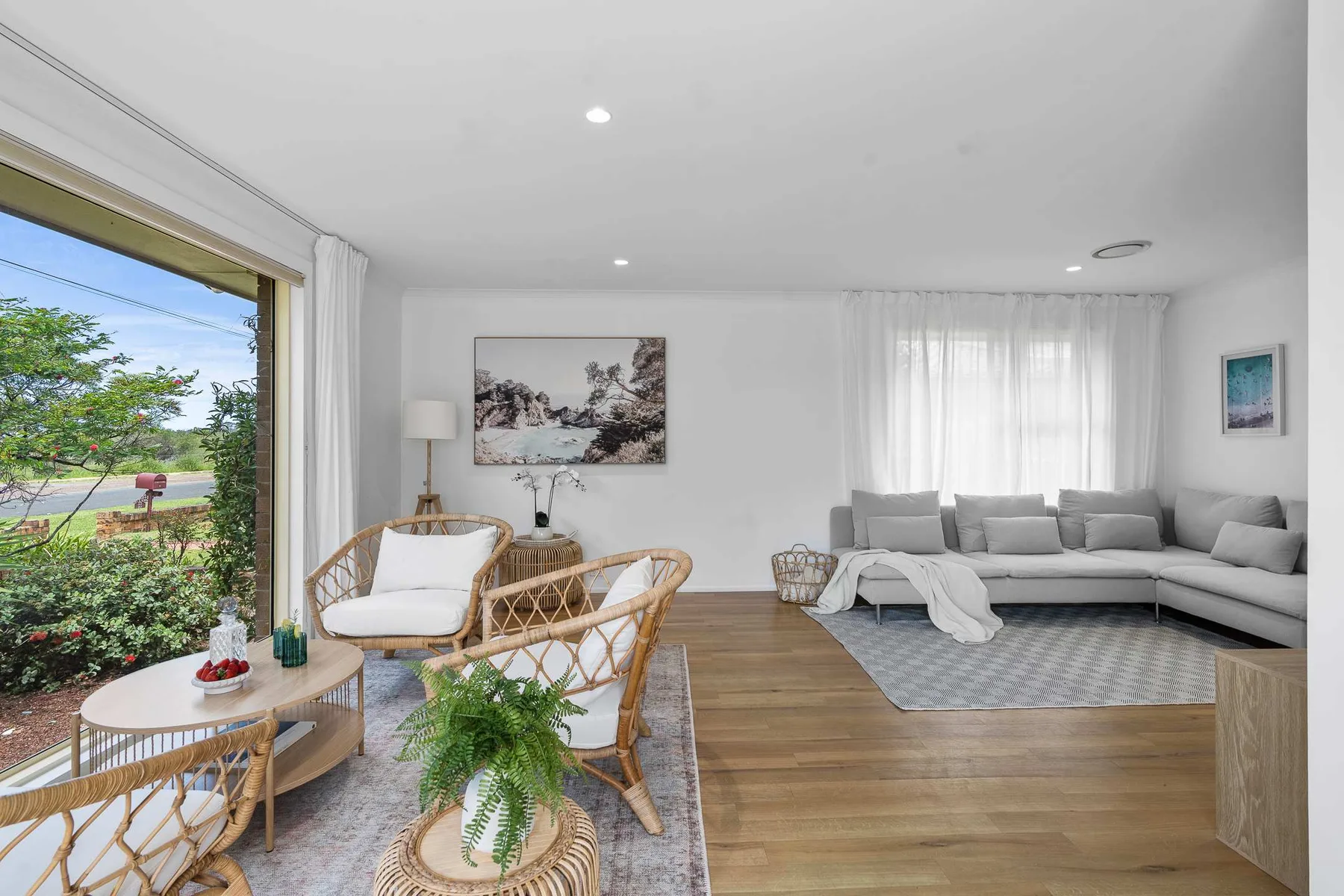 A bright living room with seating beside large windows opening onto greenery.