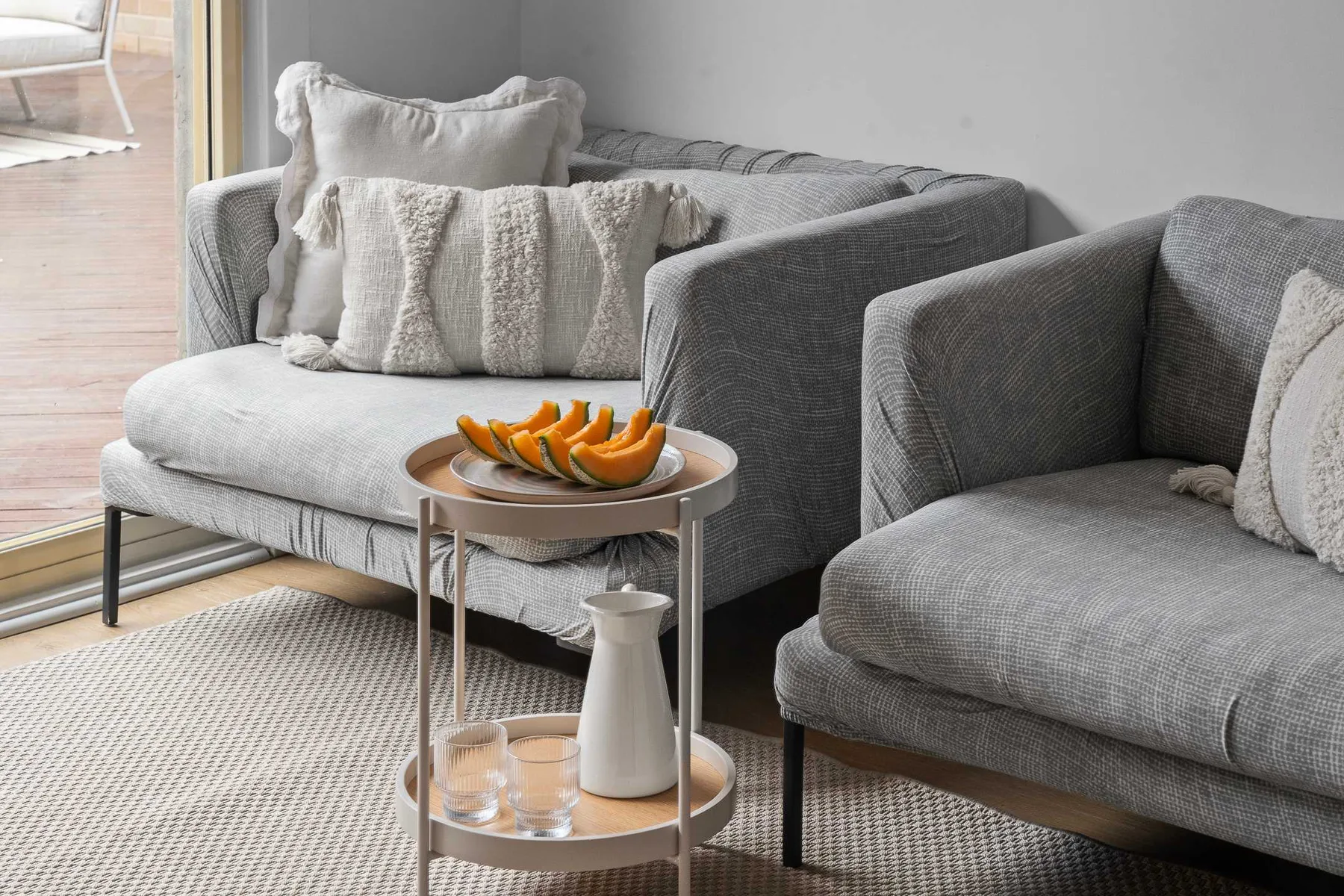 A living room with gray seating and a small table holding sliced fruit.